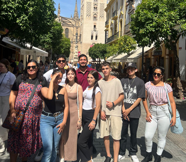 Grupo de jóvenes y personas adultas posando sonrientes en una calle peatonal del centro de una ciudad, con la Giralda de Sevilla al fondo. Parece una salida cultural o excursión organizada.